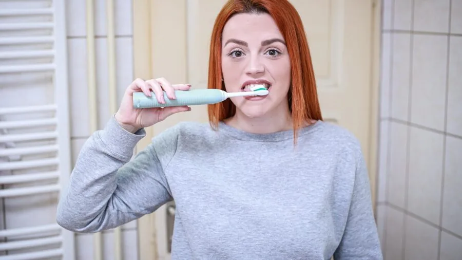 Person practicing daily oral hygiene routine with toothbrush at bathroom sink