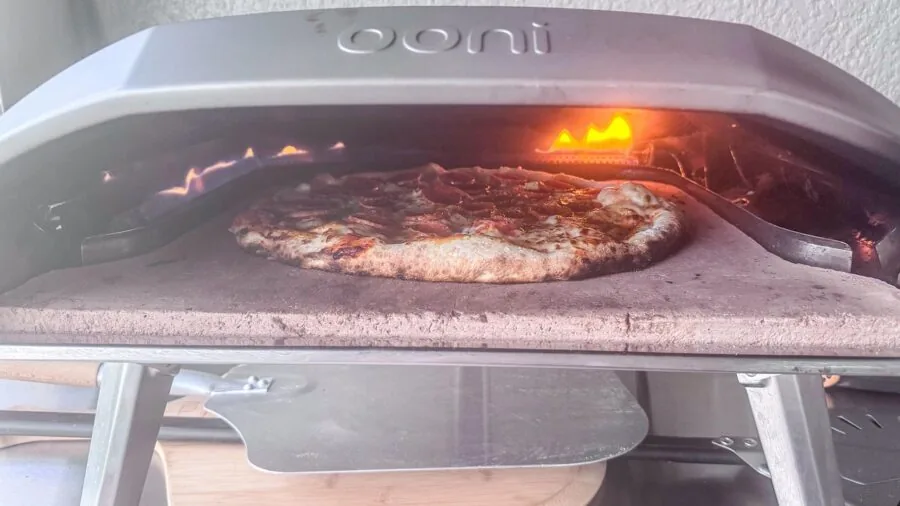 Person preparing food on outdoor grill with pizza stone during backyard gathering