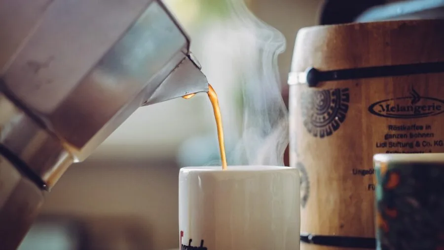 Person preparing fresh coffee in a bright kitchen with various brewing methods and cups on counter