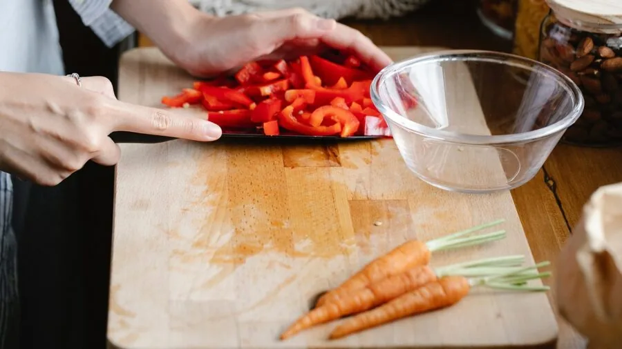Person preparing fresh vegetables on a cutting board in a bright kitchen during meal prep