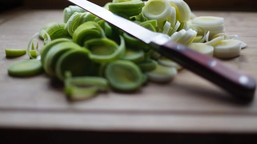 Person preparing fresh vegetables on a wooden cutting board in a bright kitchen