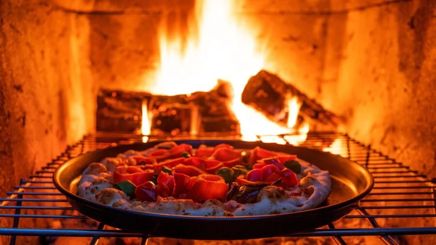Person preparing traditional Neapolitan pizza in outdoor wood-fired oven with glowing flames and hot stone interior