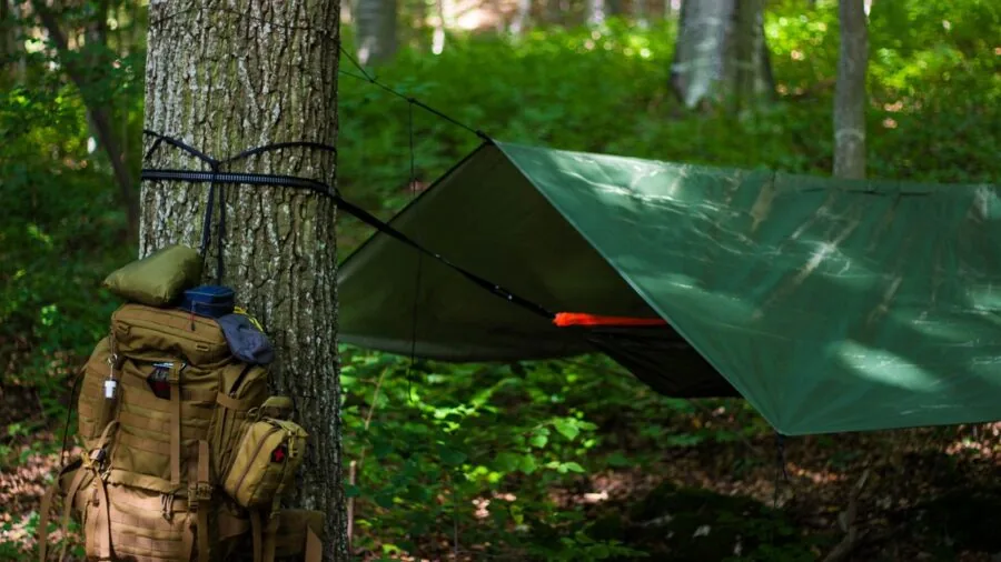 Person relaxing in hammock with bug net in wooded camping area near water