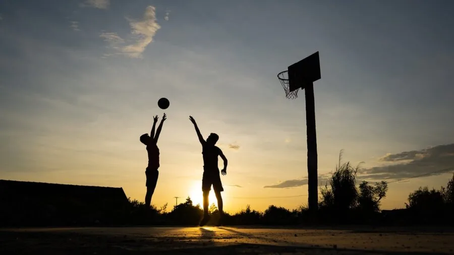Person repositioning a portable basketball hoop on a driveway in daylight