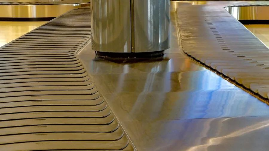 Person retrieving suitcase from airport baggage carousel in busy terminal
