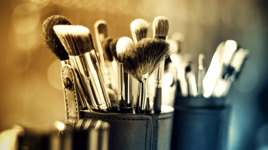 Person rinsing makeup brushes under running water in a bathroom sink for hygiene and maintenance