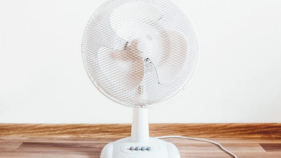 Person seated in front of oscillating fan enjoying cool air circulation in home interior