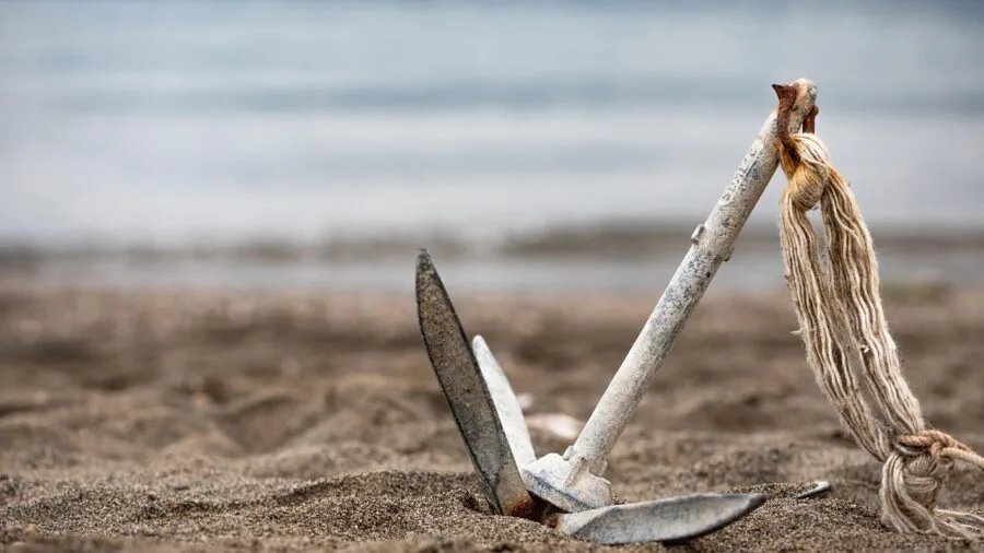 Person securing beach umbrella with sand anchor system on sandy beach