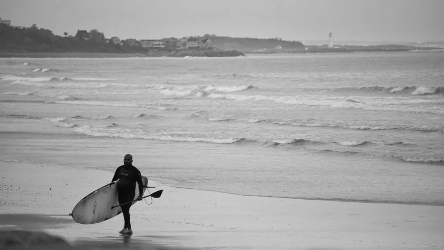 Person selecting different paddle board paddles while standing on beach near water