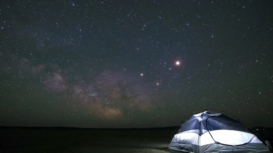 Person setting up camping gear in darkness with wide lighting illuminating the tent area
