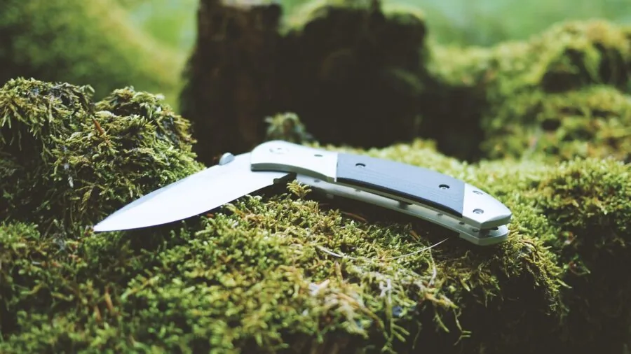 Person sharpening a camping knife outdoors on a rock during a wilderness trip