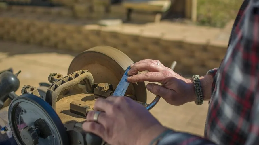 Person sharpening hunting knife blade outdoors in natural light, focusing on steel maintenance