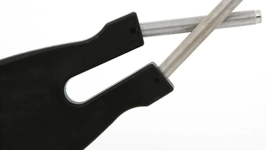 Person sharpening kitchen knife at home counter with fresh vegetables nearby