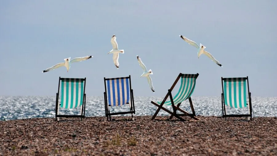 Person sitting in a lightweight aluminum beach chair on sandy beach near ocean waves