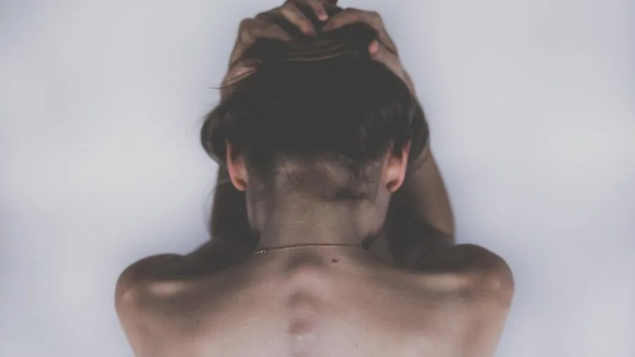 Person sitting on chair holding lower back, experiencing discomfort and tension in lumbar region