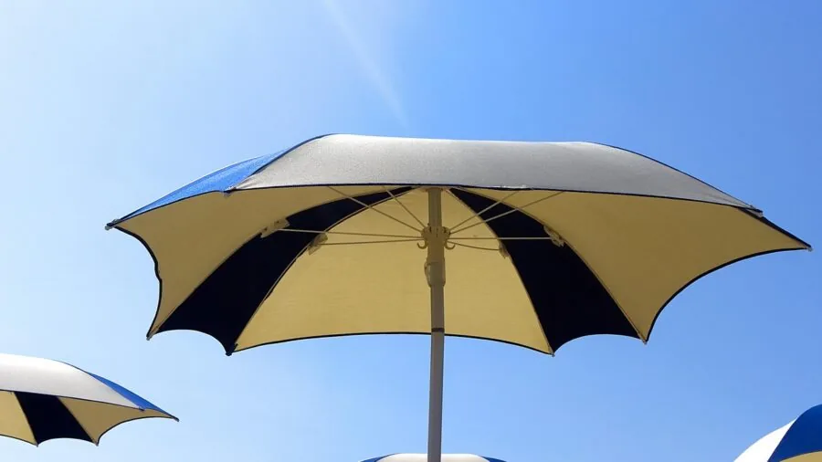 Person sitting under beach umbrella enjoying shade on sandy beach during sunny day