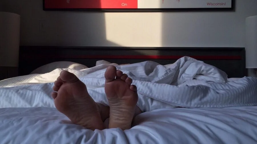 Person sleeping comfortably in bed during morning light, showing quality bedding and restful sleep
