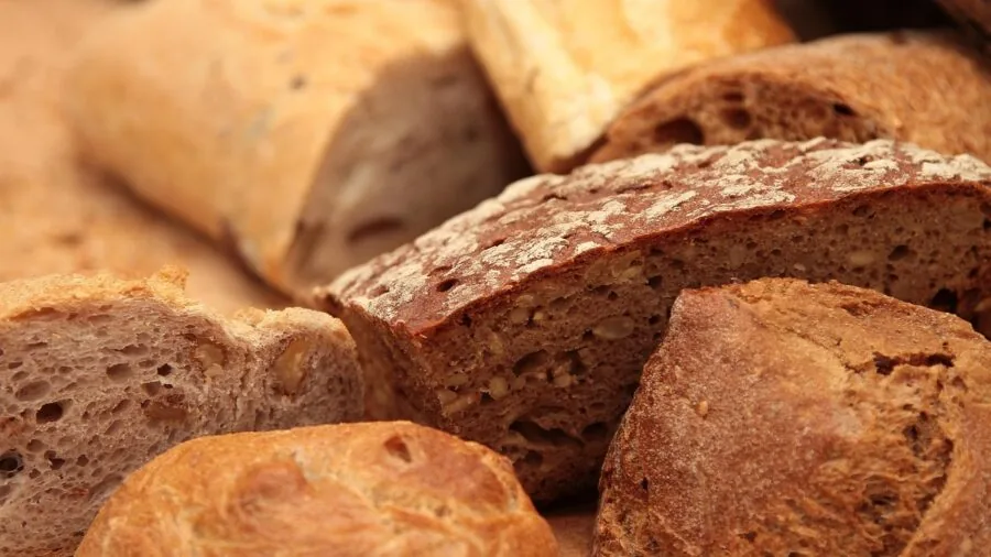 Person slicing fresh crusty bread on wooden cutting board in home kitchen
