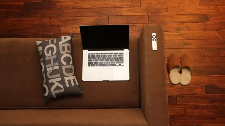 Person sliding a gray sofa across hardwood flooring in a bright living room during furniture rearrangement