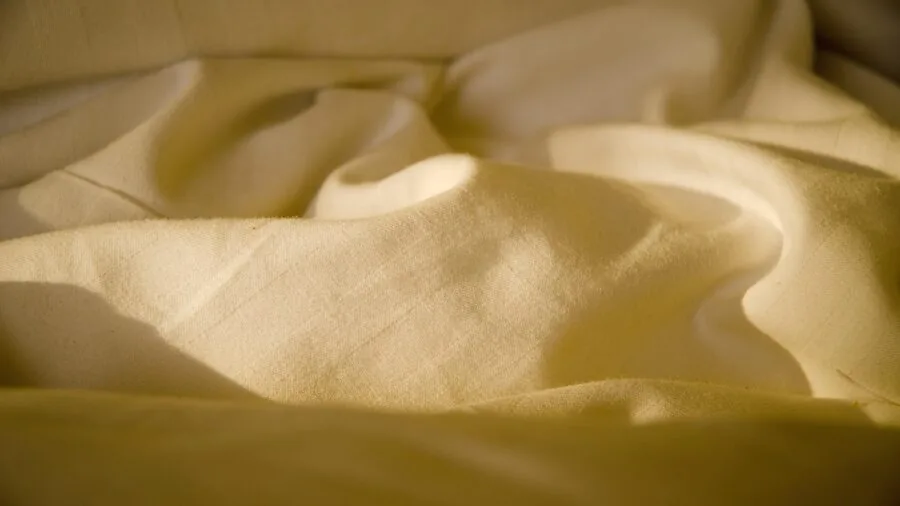Person smoothing and adjusting white bed sheets on mattress during morning bedroom routine