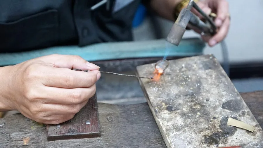 Person soldering electronic components at a wooden workbench with tools and circuit boards in natural light