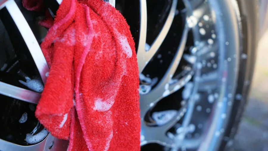 Person spraying and cleaning car tires in driveway, preparing vehicle for drive