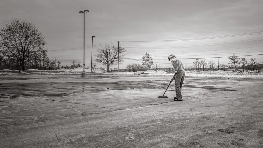 Person sweeping concrete driveway with stiff bristle broom on sunny day
