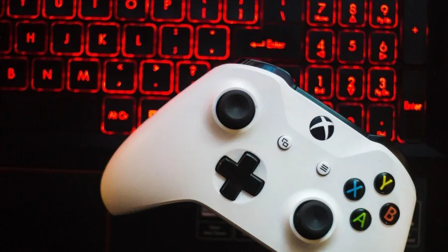 Person toggling between gaming console and laptop during gameplay session at desk