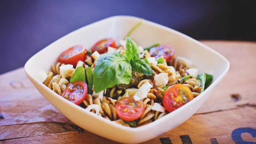 Person tossing fresh salad in a wide shallow ceramic bowl on a kitchen table