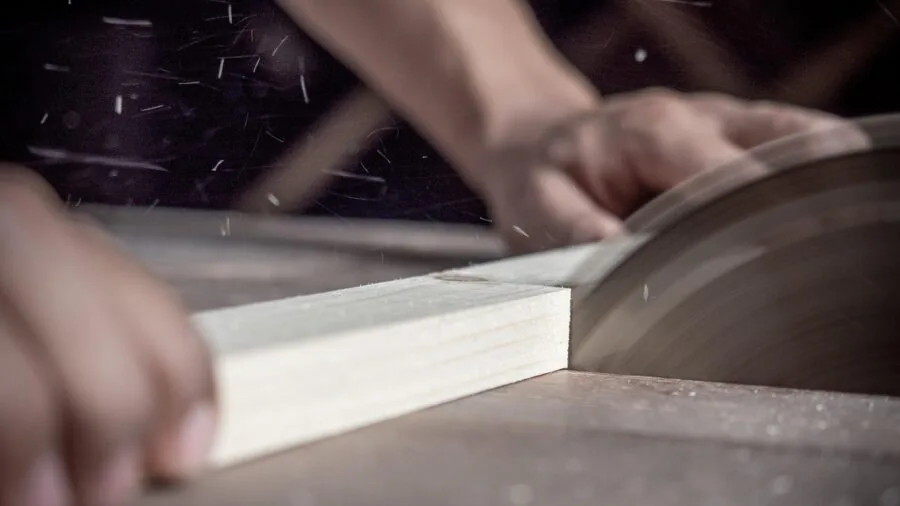 Person using a hand saw to cut wood during a carpentry project in a workshop setting