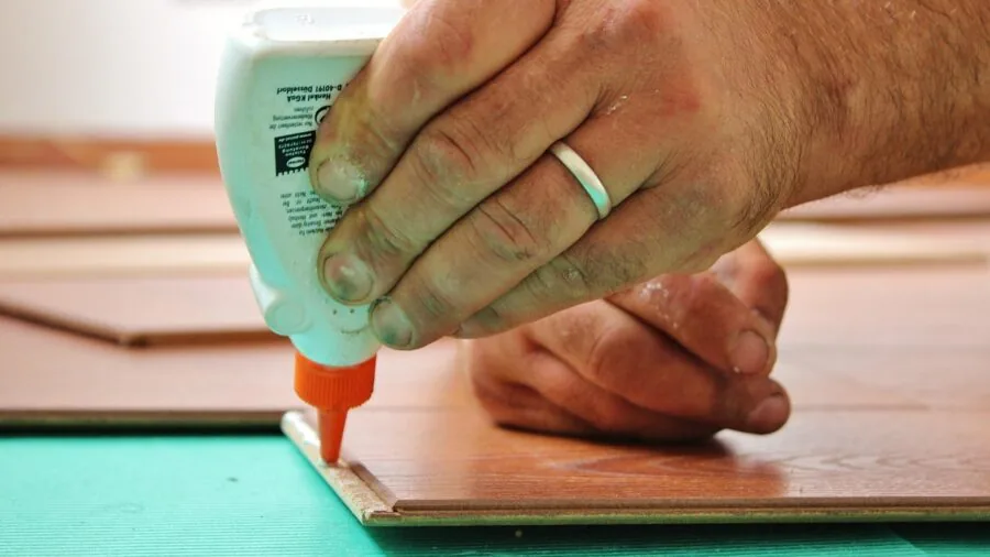 Person using a hot glue gun on a craft project at a wooden worktable with materials