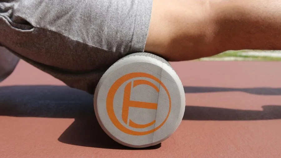 Person using a standard foam roller during a home fitness routine on a wooden floor