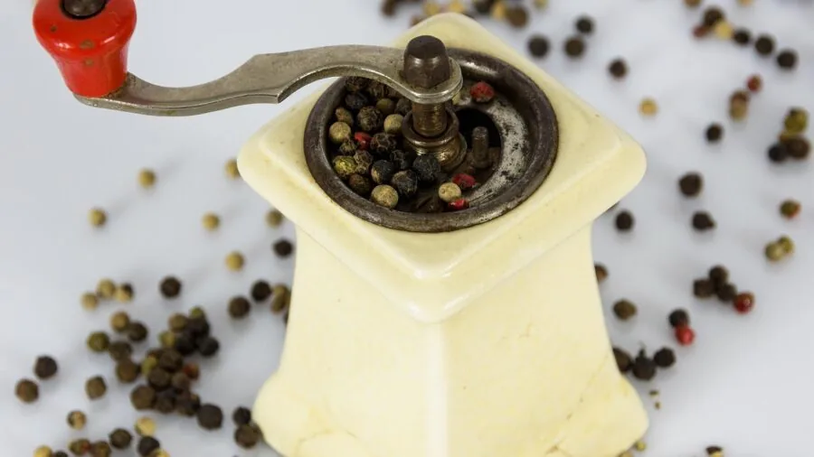 Person using manual pepper mill while cooking in kitchen, demonstrating tactile control and precision grinding technique