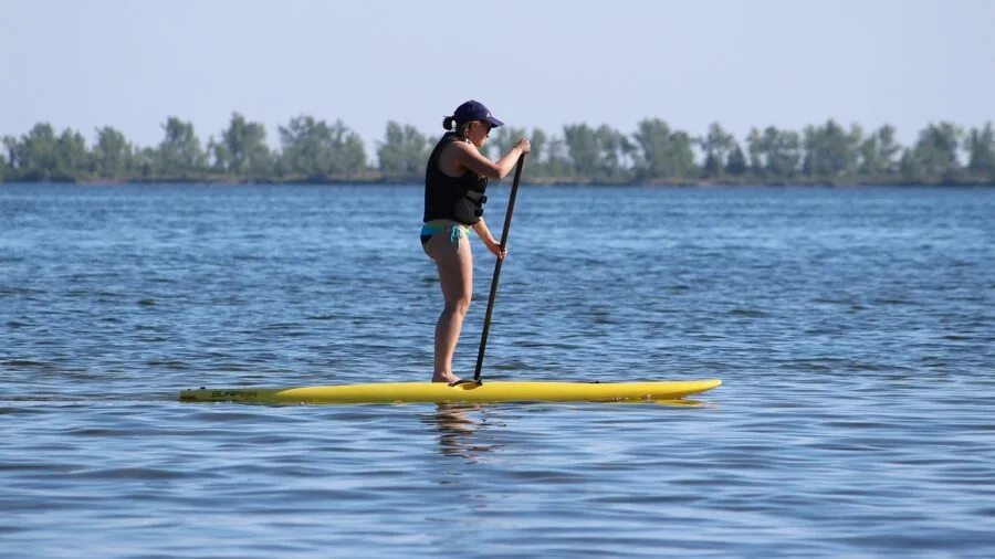 Person using pump to inflate paddle board by lake shore before paddling session