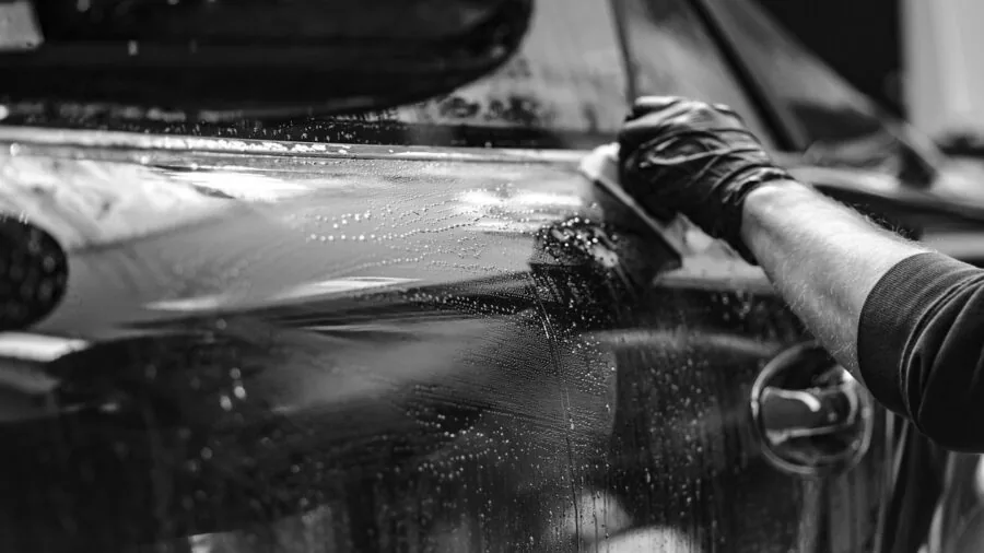 Person washing a car with a microfiber wash mitt, showing proper cleaning technique and water splash