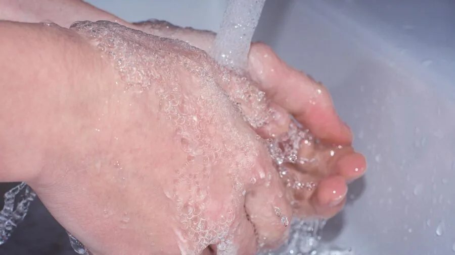 Person washing a ceramic bowl under running water in a kitchen sink, demonstrating proper cleaning technique
