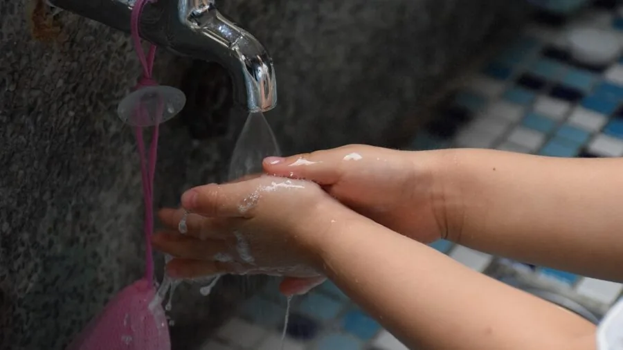 Person washing a griddle pan with warm soapy water in a kitchen sink under running water