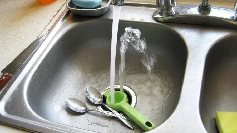 Person washing and cleaning stainless steel cookware in bright kitchen sink with natural light