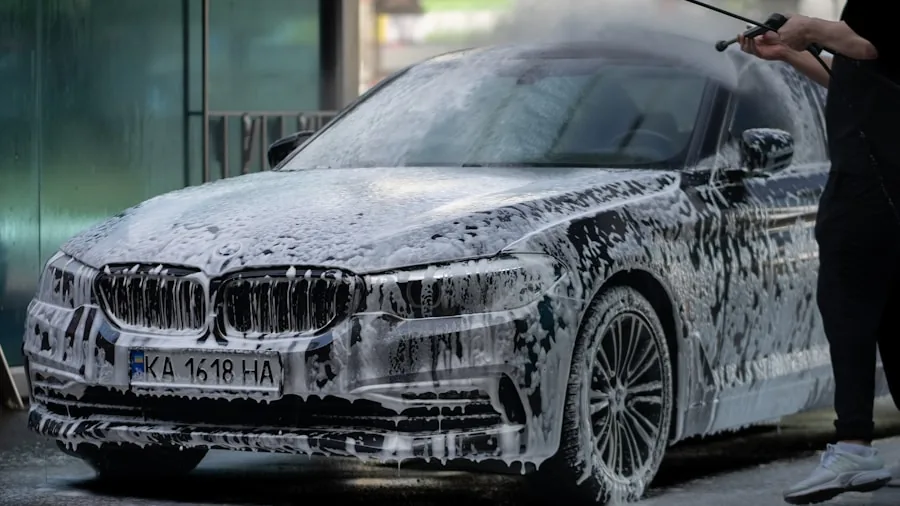 Person washing car with soap foam using bucket method in driveway on sunny day