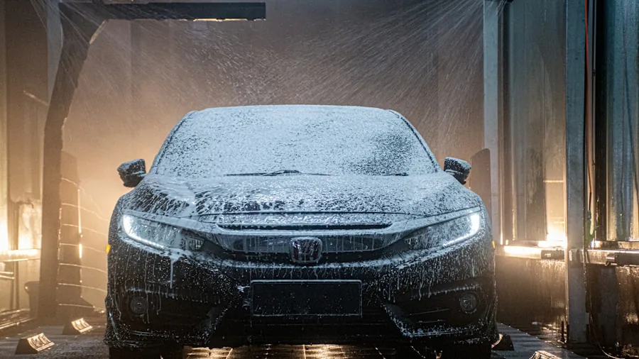 Person washing car with thick white foam and wash mitt in sunny driveway