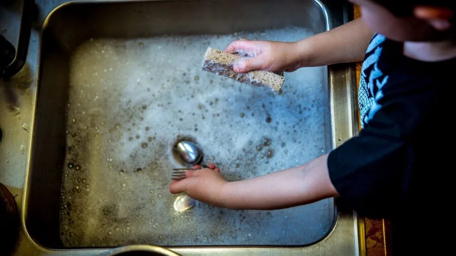 Person washing dishes by hand in a modern kitchen sink with stainless steel faucet