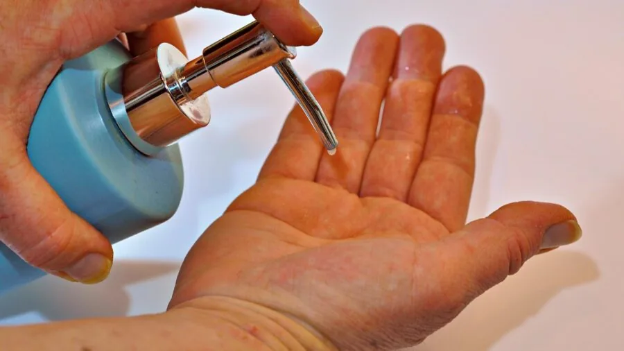 Person washing hands under running water in a bright, clean bathroom setting