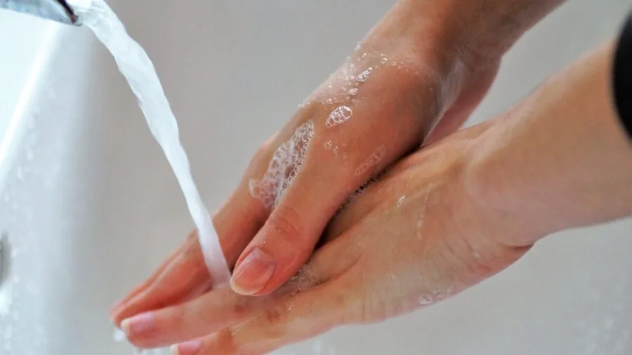 Person washing hands with soap and water at sink, demonstrating daily handwashing routine