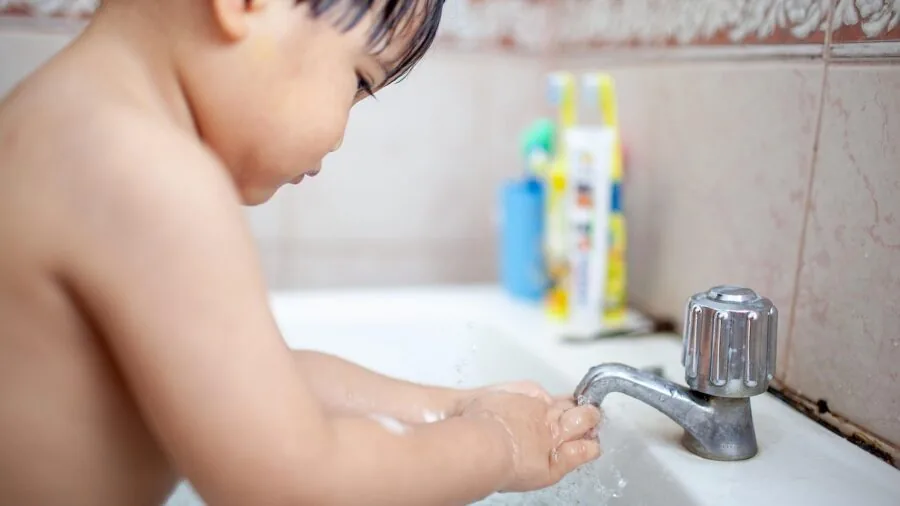 Person washing kitchen utensils under running water in a bright, clean kitchen sink with natural light