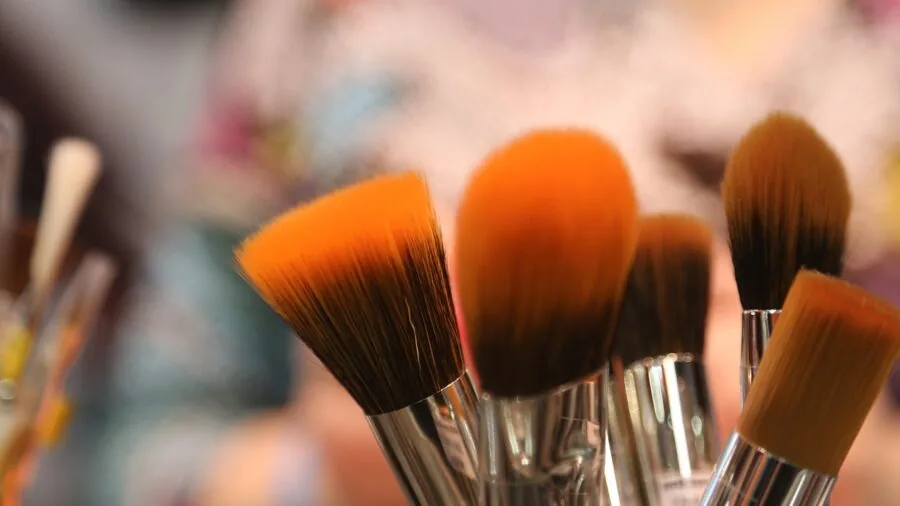 Person washing makeup brushes and sponges in sink with water, emphasizing beauty product care and reusability