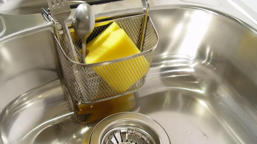 Person washing nonstick cooking equipment in kitchen sink with soapy water