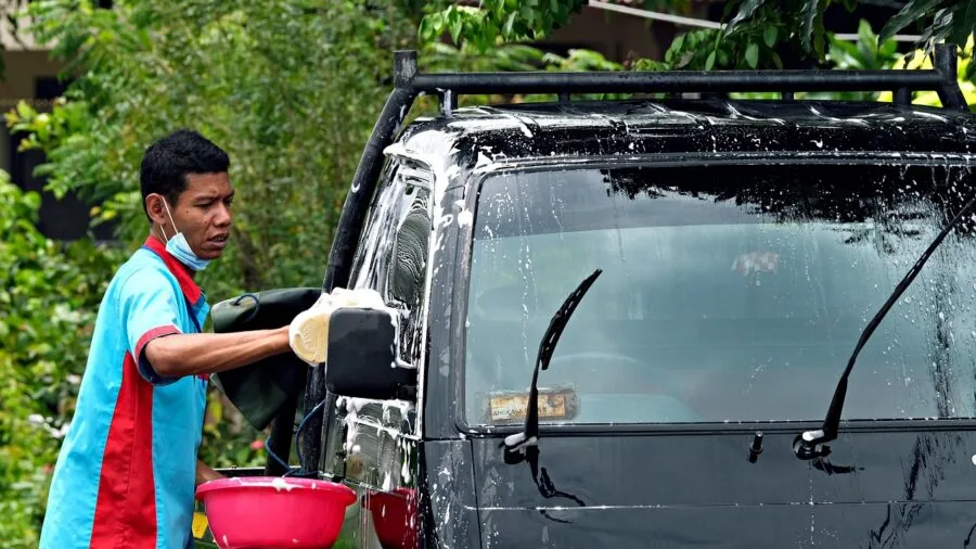 Person washing their car with water and sponge in driveway on sunny day