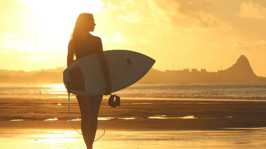 Person waxing a surfboard on sandy beach before surfing in ocean water