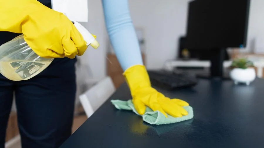 Person wiping down a laundry basket with a damp cloth during household cleaning routine
