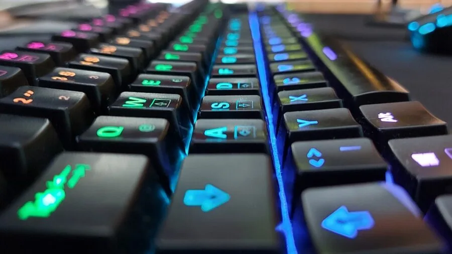 Person working at desk with vibrant RGB keyboard backlighting in dark room setup